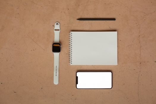 Top-down view showcasing smartwatch, smartphone, notebook, and pen on a neutral background.