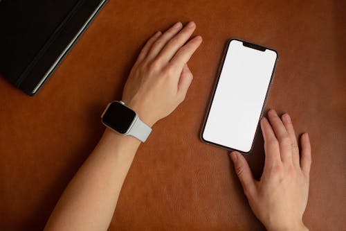 A Person Wearing a Smartwatch Touching a Smartphone with a Blank Screen
