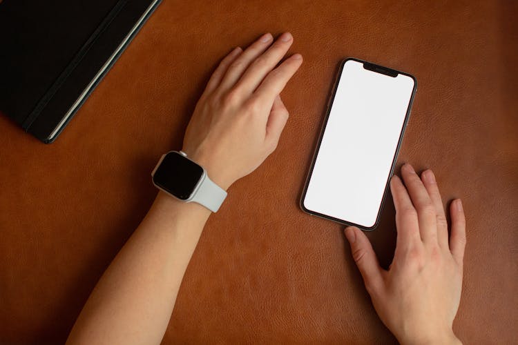 A Person Wearing A Smartwatch Touching A Smartphone With A Blank Screen
