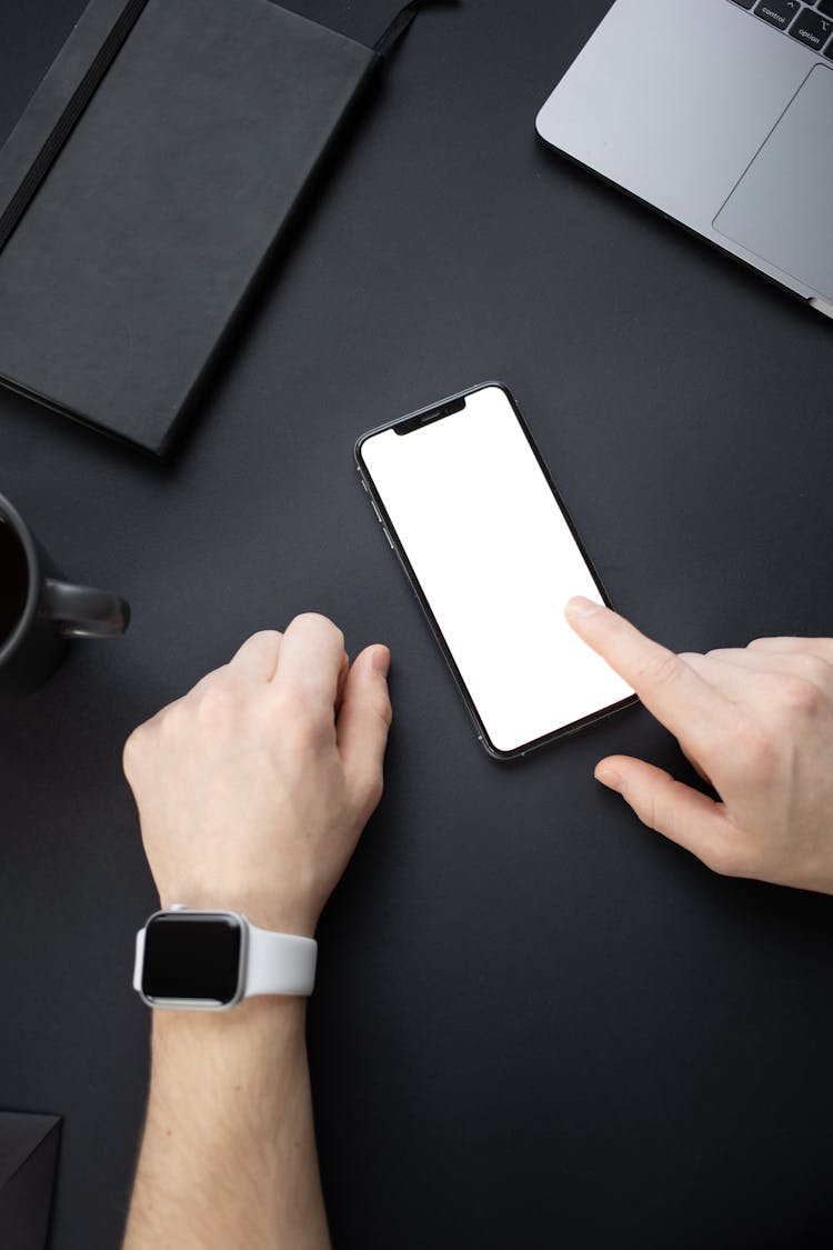 A Person Wearing A Smartwatch Touching The Blank Screen Of A Smartphone 
