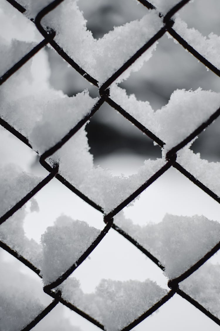 A Snow Covered Chain Link Fence With Snow In Close-Up Photography