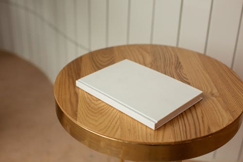Free From above of round shaped wooden table with blank white book on blurred background Stock Photo
