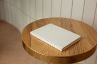 From above of round shaped wooden table with blank white book on blurred background