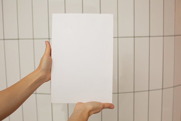 Person Holding Blank Board In Front Of White Wall