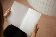 High angle of crop unrecognizable female looking on blank sheets of paper while sitting in light room