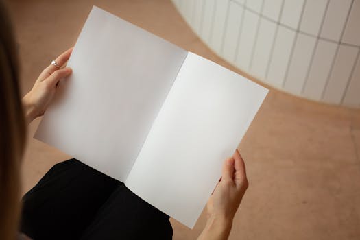High angle of crop unrecognizable female looking on blank sheets of paper while sitting in light room