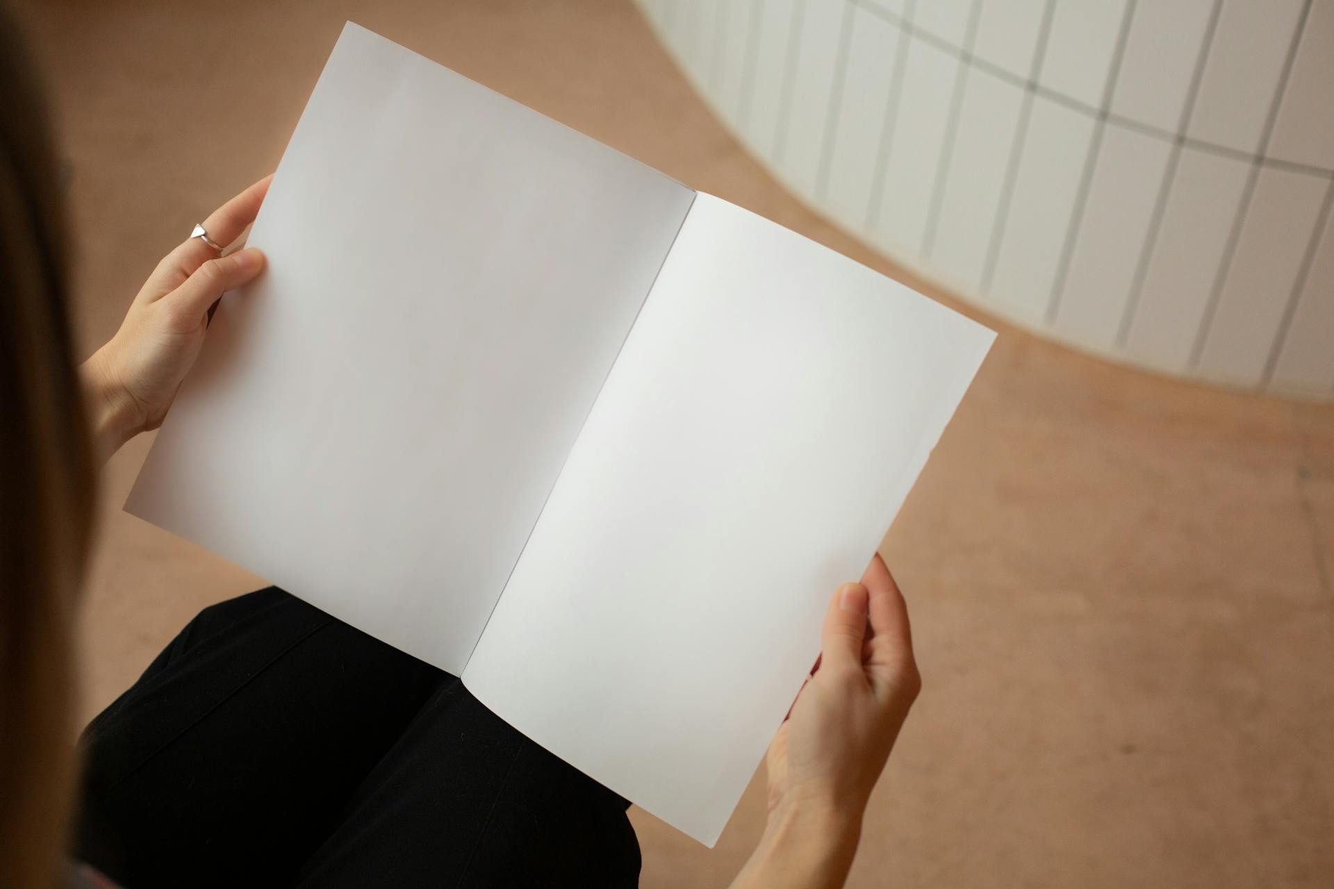 High angle of crop unrecognizable female looking on blank sheets of paper while sitting in light room