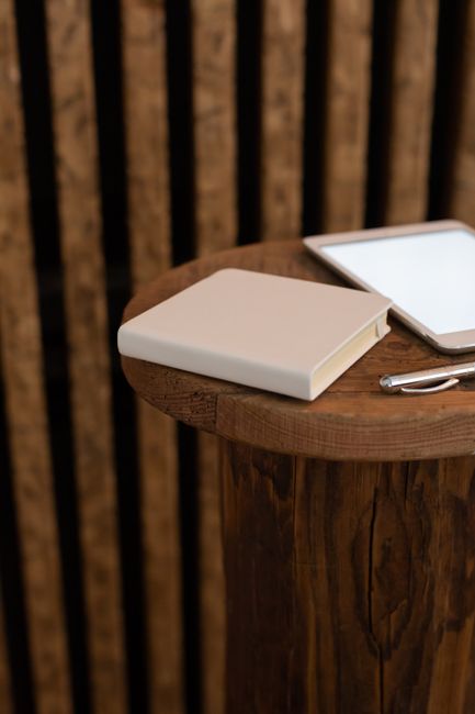 High angle of mockup of book with beige cover and tablet with empty screen placed on round wooden table on striped background