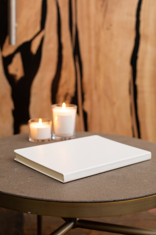 White blank notepad with hardcover placed on round table with burning candles near wall in light modern room at home