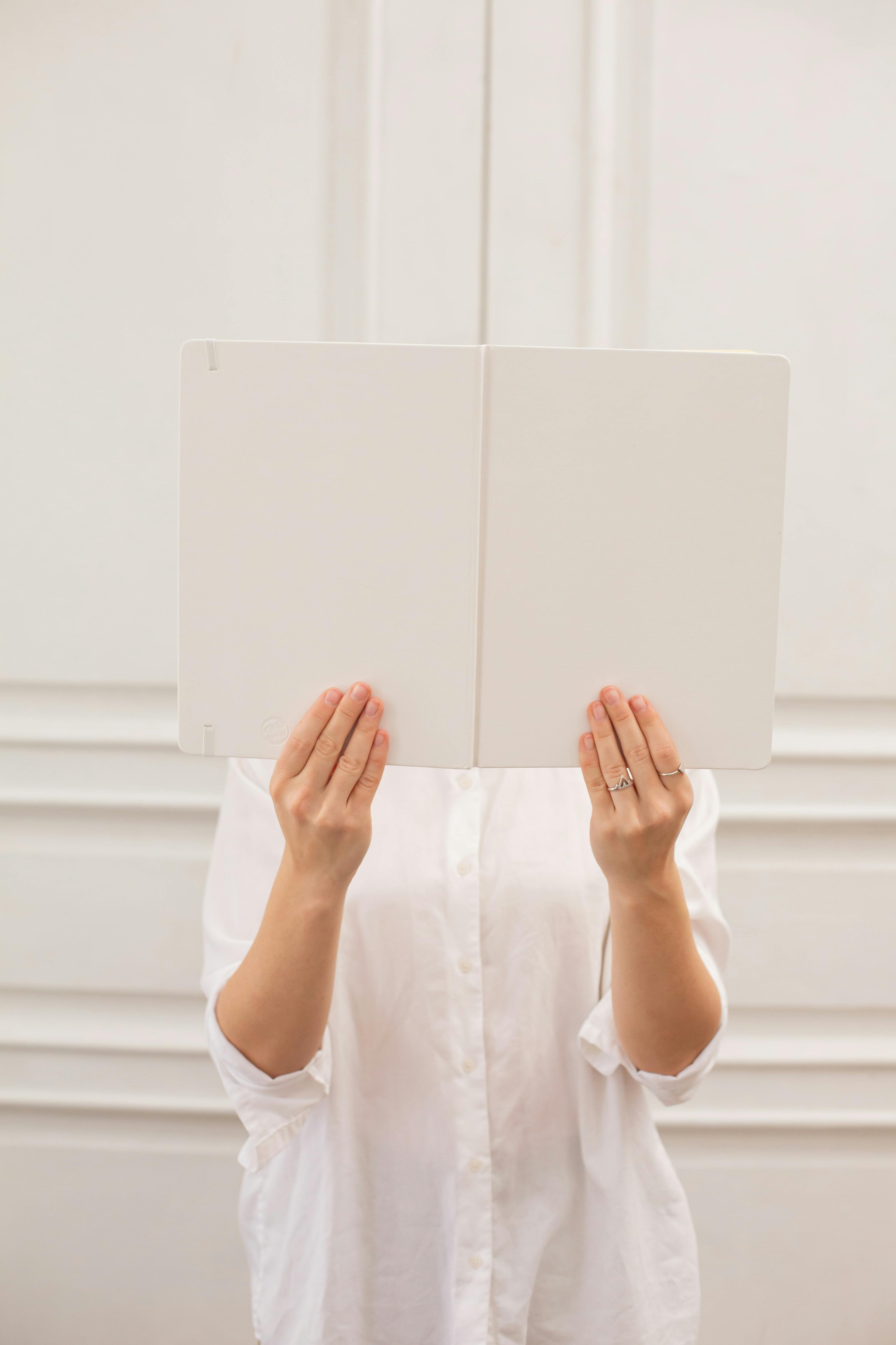 unrecognizable woman covering face behind blank book