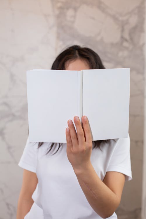 Free Anonymous woman covering face with mock up notepad Stock Photo