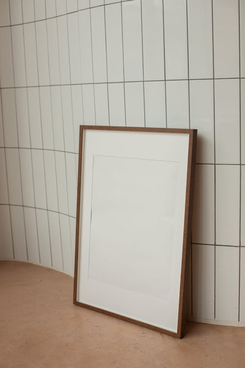 Blank rectangular shaped frame with brown border placed on floor near wall with white tiles in light room at home