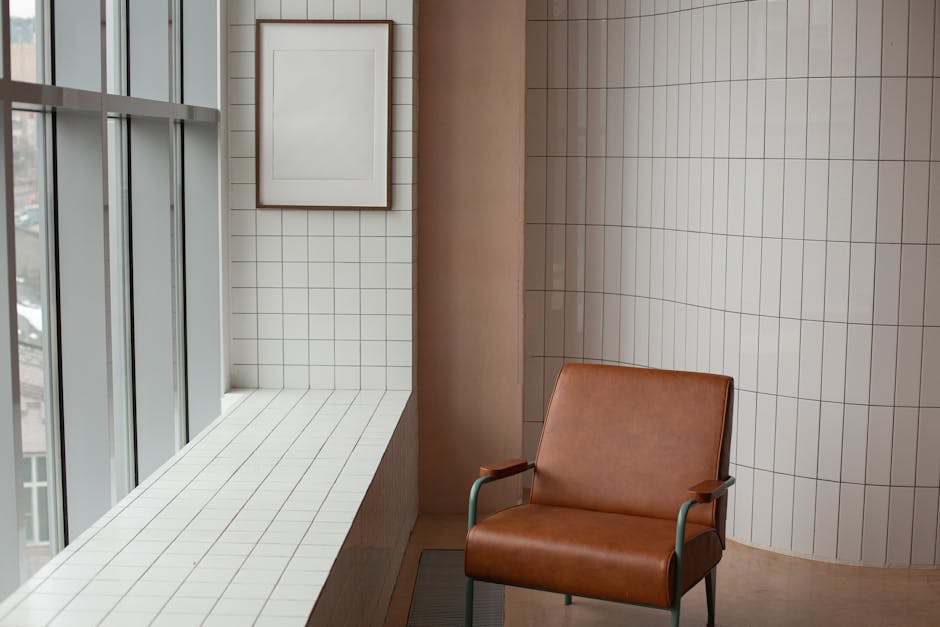 Brown armchair placed near mock up frame hanging near window and windowsill in small room with tiled walls at home