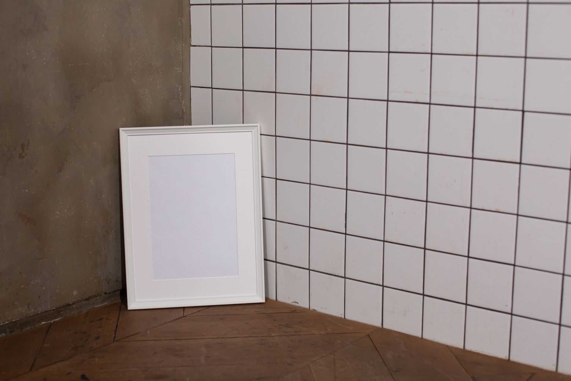Empty white photo frame placed on parquet in room corner against tiled wall