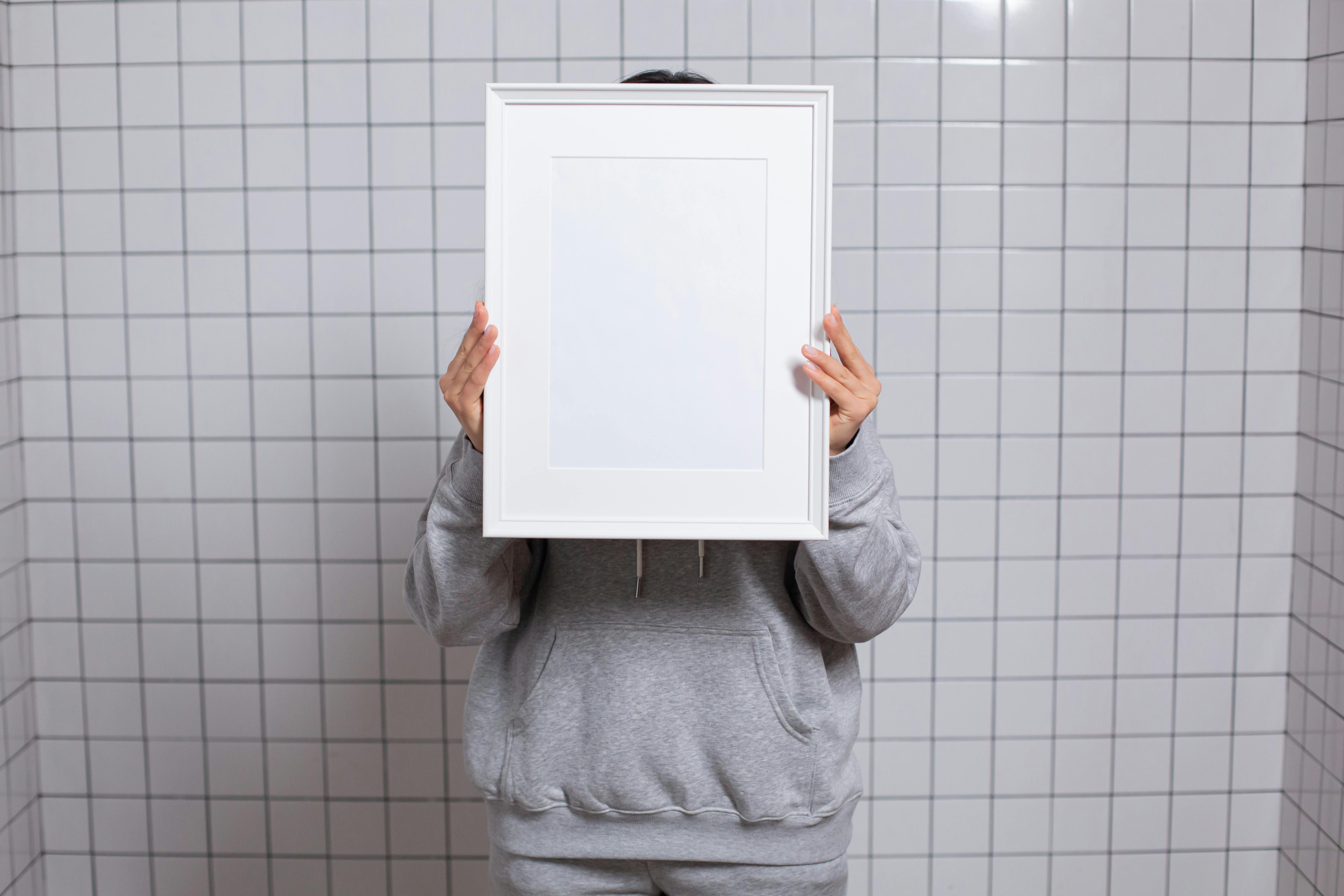 faceless person covering face with empty photo frame