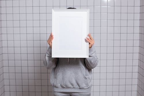 Faceless person covering face with empty photo frame