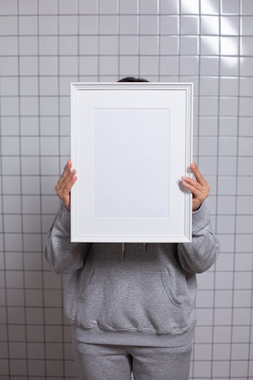 Anonymous person covering face with empty white photo frame
