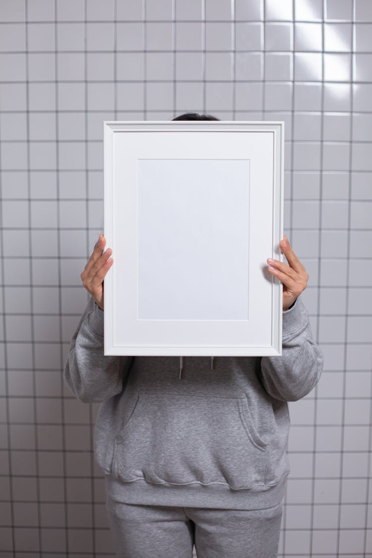 Anonymous Person Covering Face With Empty White Photo Frame