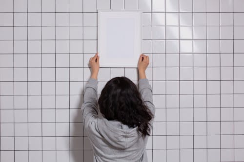 Unrecognizable woman hanging empty photo frame on tiled wall