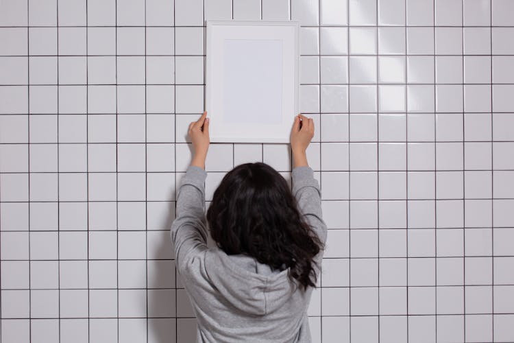 Unrecognizable Woman Hanging Empty Photo Frame On Tiled Wall