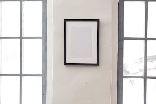 Interior of simple apartment with blank frame on white wall between rectangular shaped windows