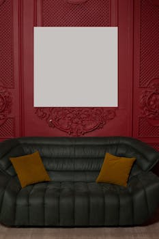 Empty white paint hanging on red wall above leather sofa with pillows in stylish apartment