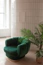 Empty light room with green armchair near potted plant and white canvas placed on tile wall near window