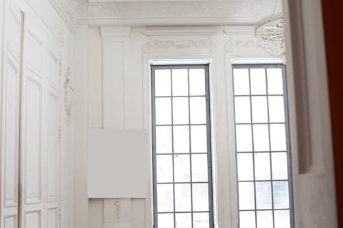 White square board placed on wall with ornamental elements near windows and chandelier on ceiling in bright room