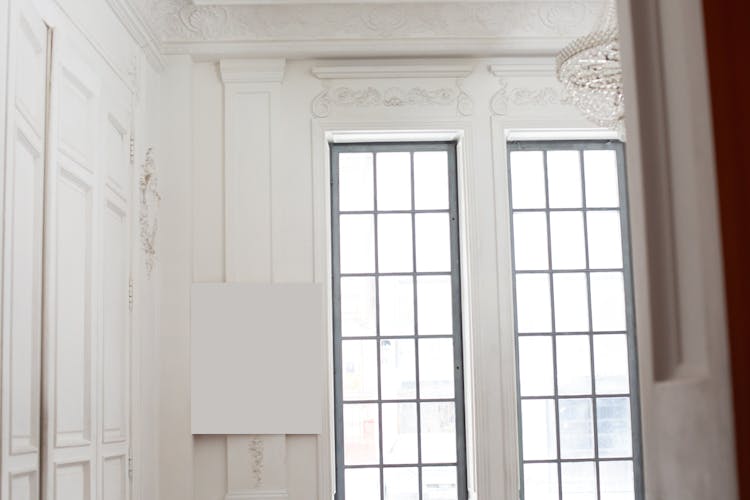 White Canvas On Wall With Ornaments Near Windows In Room