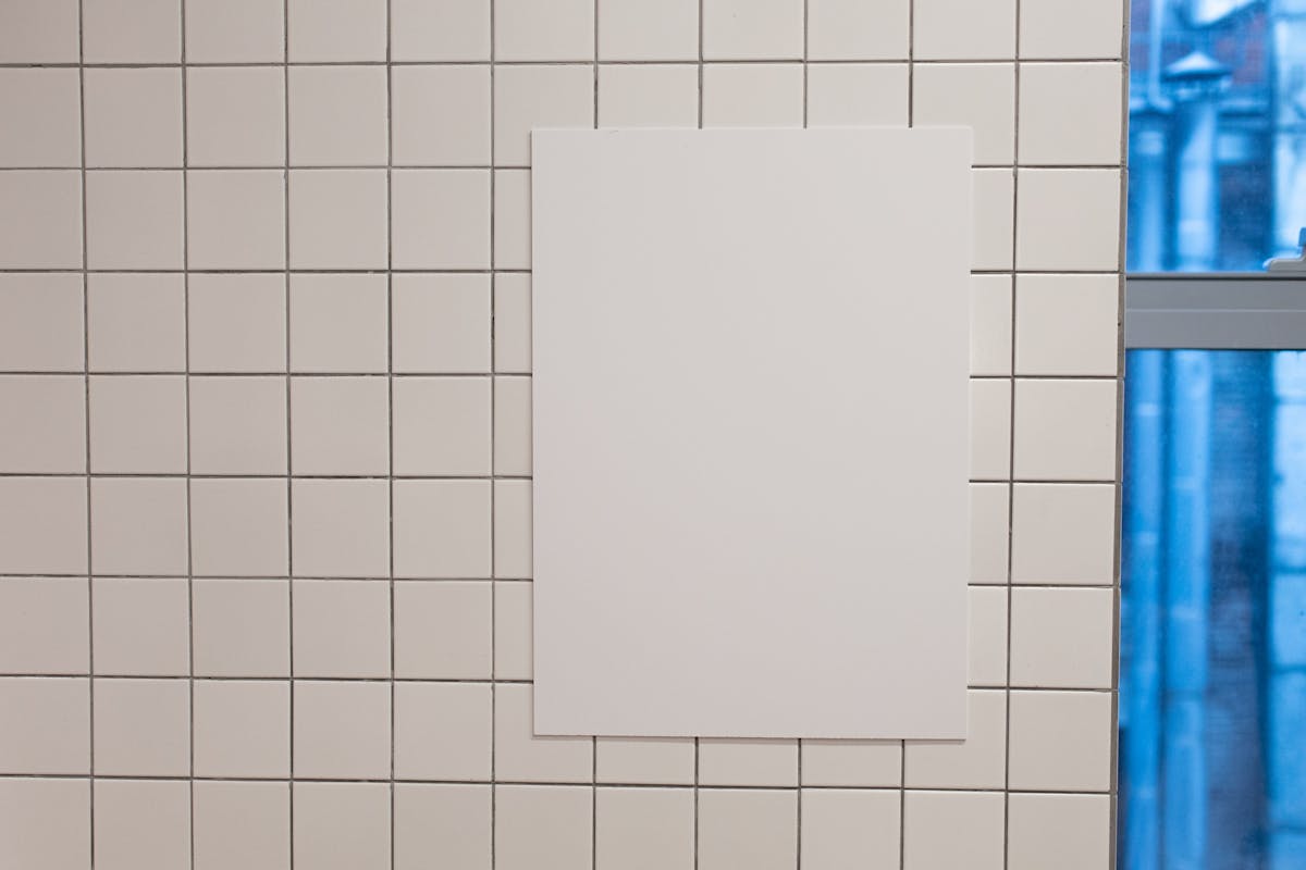 Blank white placard hanging on wall covered with white tiles inside of building