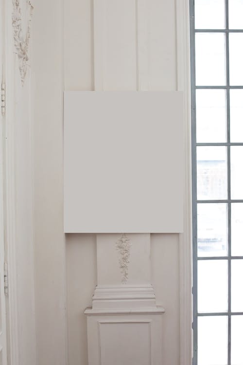 Blank white frame hanging at corner on wall with post and classic decorative elements near big window in light room