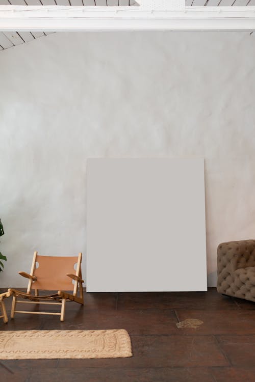 White mock up poster with copy space at wall in light furnished room with armchair and couch in modern studio