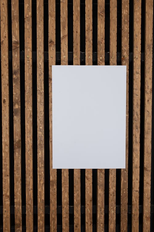 Full frame of blank white paper sheet hanging on decorated wall with wooden planks in light room of modern studio