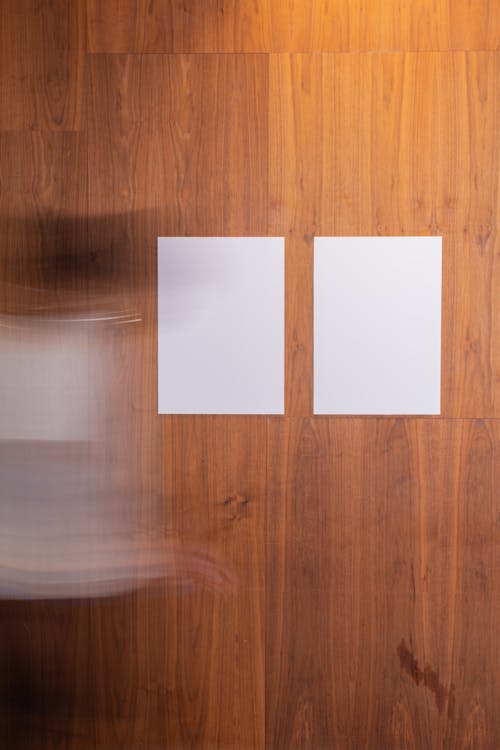Faceless blurred person in motion strolling along wooden wall with creative rectangular white blank posters in light room in studio