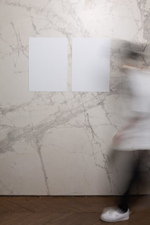 Side view of faceless person in motion wearing casual clothes strolling along marble wall with white mock up rectangular placards