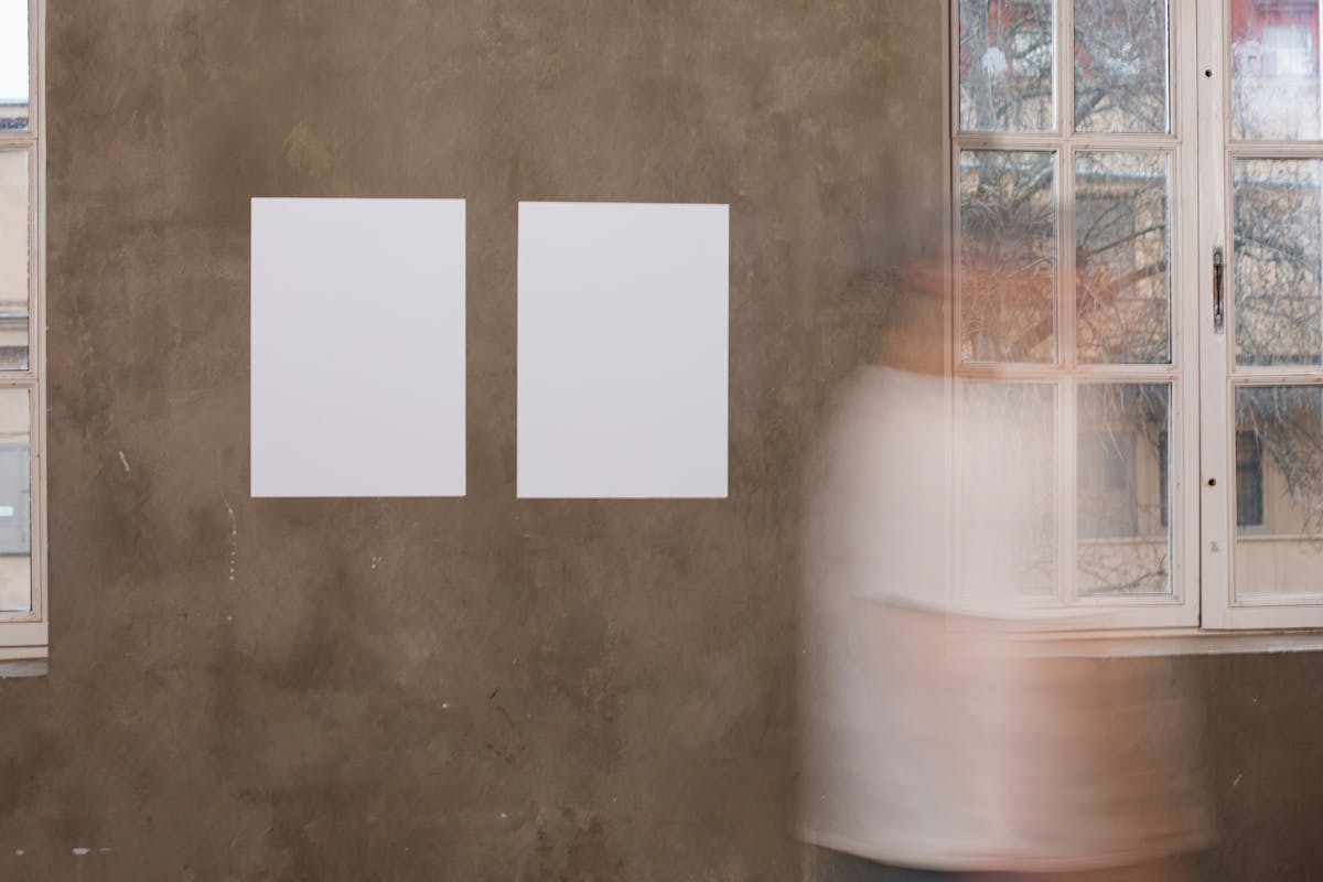 Side view of unrecognizable person in motion strolling along mock up placards hanging on wall in light room with windows