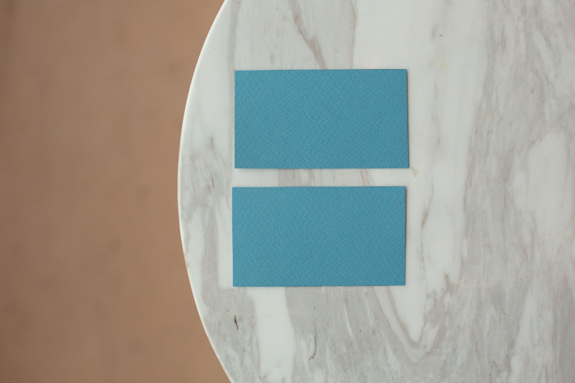 Two blue business cards placed on a white marble surface viewed from above.