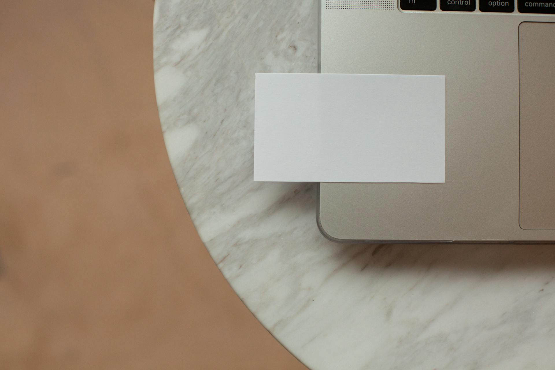 Top view white mock up business card with copy space placed on modern opened netbook on round marble table in light room