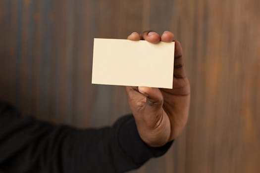 A close-up shot of an unrecognizable man holding a blank business card against a wooden background.