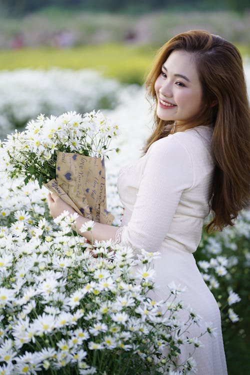 Side view of cheerful young ethnic female with blossoming floral bouquet looking away in field