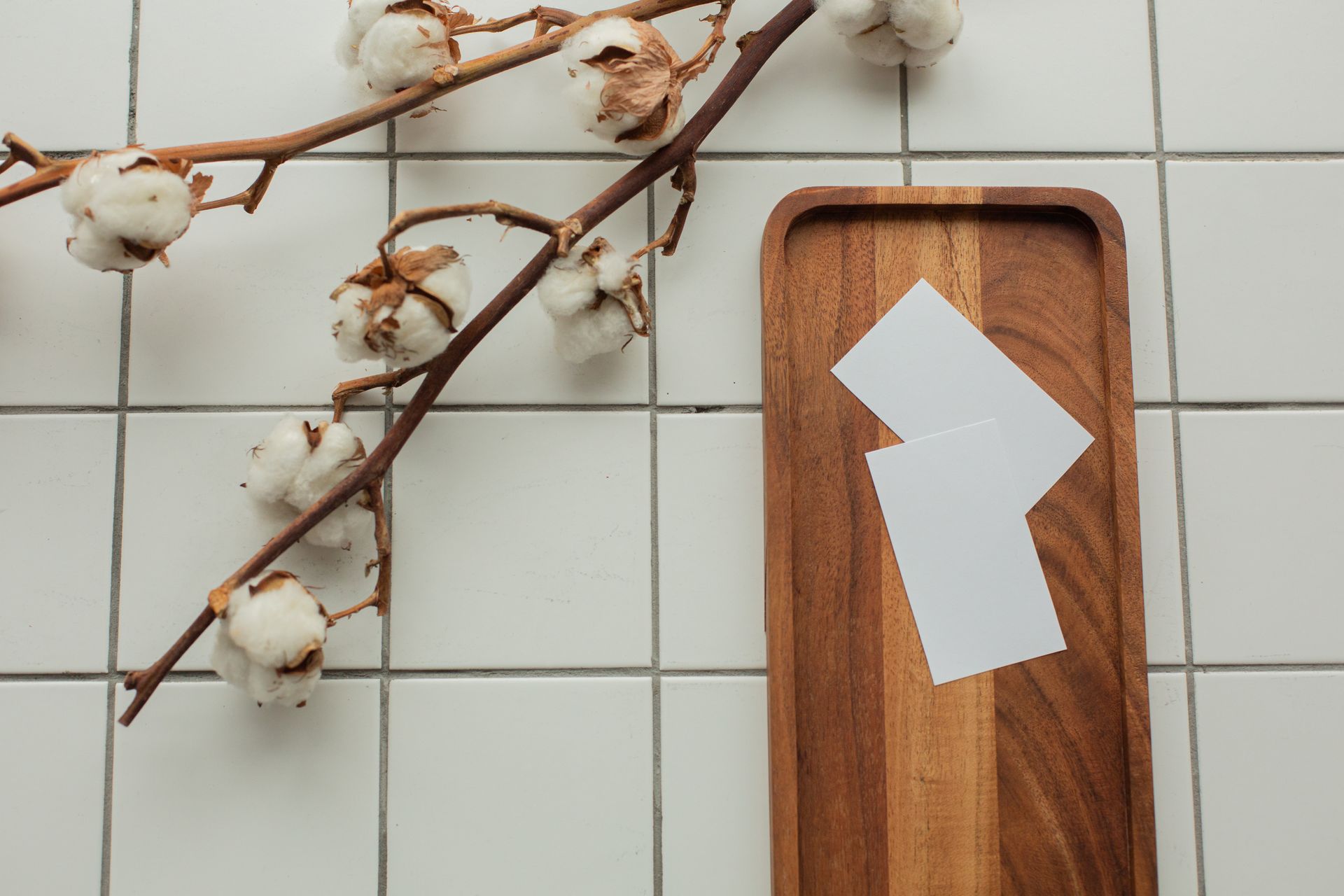 Top view of white mock up business cards on wooden tray on tiled floor near cotton flowers in light room