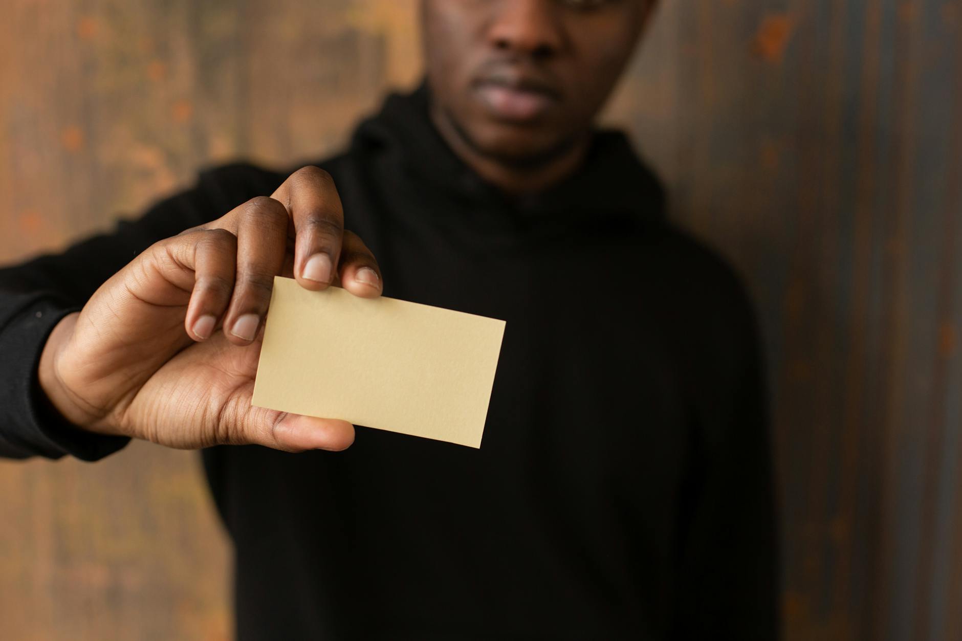 Faceless man in a dark hoodie holds a blank business card, offering ideal copy space.