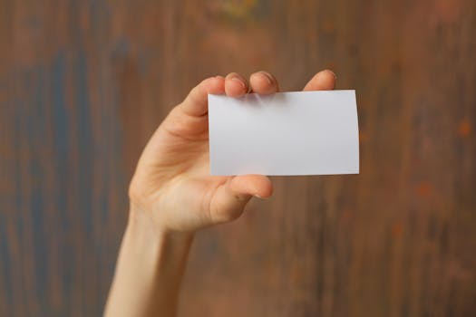 Human hand holding blank white card with wooden background focus on card