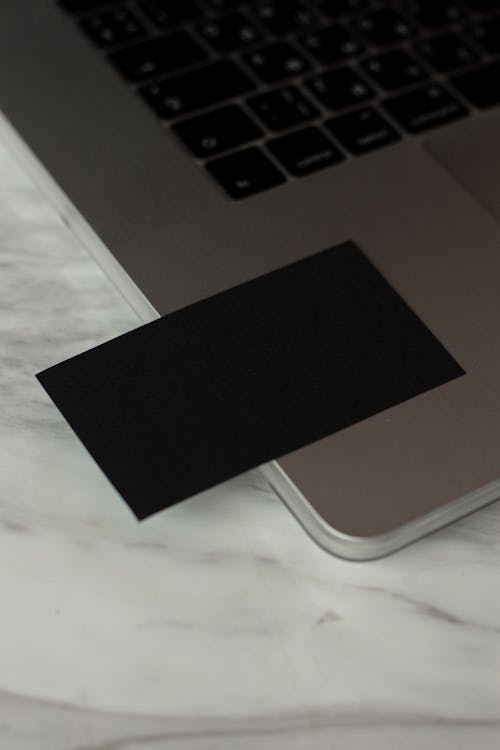 From above of blank black business card with copy space placed om contemporary opened computer on table in modern workspace