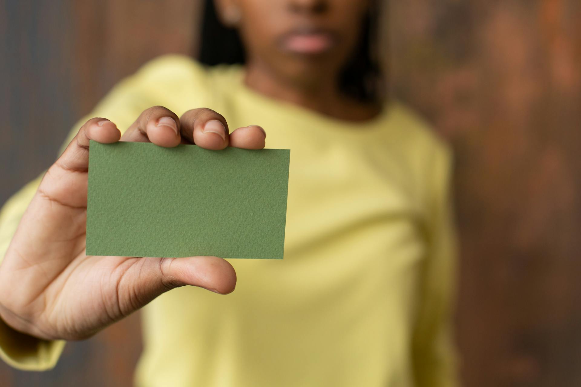 An unrecognizable woman holds a blank green card indoors, offering ample copyspace.