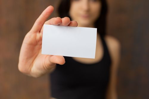 Free Soft focus of unrecognizable female in casual clothes demonstrating white mock up business card with copy space while standing near wall Stock Photo
