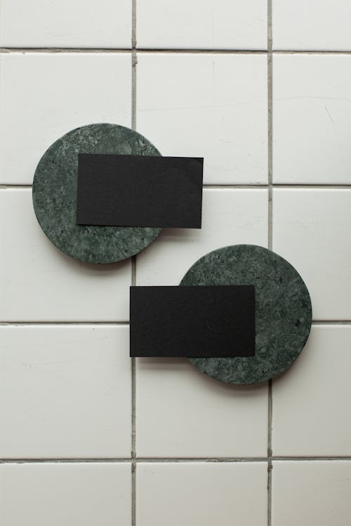 Top view of black mock up business cards on green round coasters placed on tiled floor in light room of studio