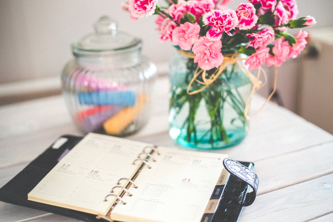 Free Personal organizer and pink flowers on desk Stock Photo