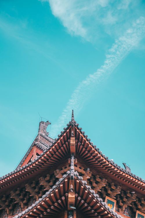 Free Low-angle view of a traditional Asian temple roof framing against a clear blue sky, capturing cultural essence. Stock Photo