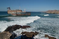 一艘腐烂的沉船在岩石海岸边生锈，是在晴朗的日光下拍摄的